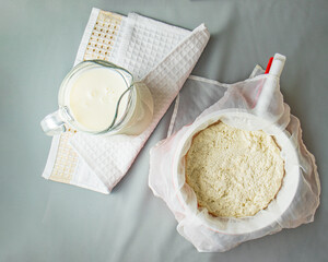 Fresh ricotta cheese in a white sieve and milk in a glass jug, and kitchen towel , Soft ricotta cheese, cooking process , process of making home-made cheese in the workshop, Cheese for package design 