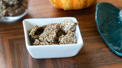 Homemade seed crackers in a white square bowl and in a jar on a wooden table.