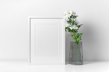 Blank frame mockup in white room interior wih flowers decorations