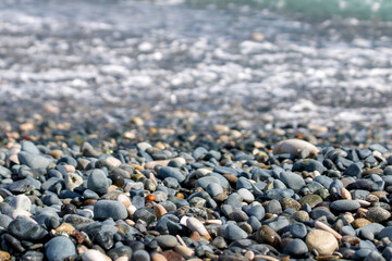 Fototapeta na wymiar Beach stones and pebbles in front of blurry sea water