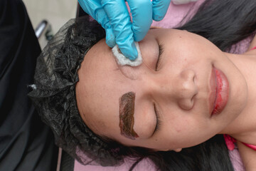 An esthetician wipes off excess pigment from the eyebrows of a customer with a ball of cotton. Example of Microblading procedure.