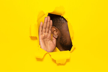 Eavesdropping. Unrecognizable black guy putting ear to torn yellow paper background, listening...