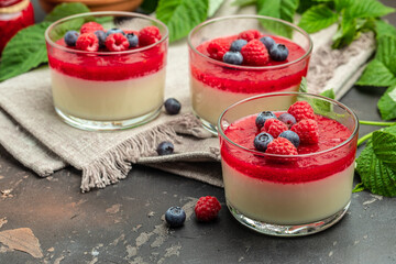 Delicious italian dessert panna cotta with berry sauce on a dark background in small jars. place for text - obrazy, fototapety, plakaty