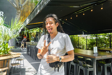 young man with dreadlocks standing outside a restaurant looking at the camera making a v sign