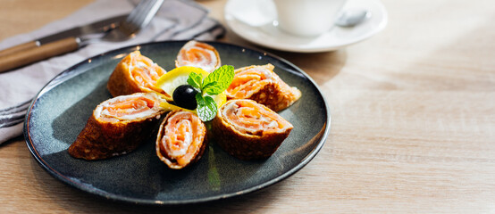 Delicious thin pancakes withsmoked salmon and cream cheese on light wooden table. Morning breakfast concept. Copy space. Banner for design, website.