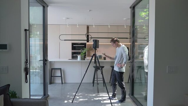 Wide shot of floor plan specialist walking towards matterport device in modern home, measuring equipment. Real estate marketing service of bright sunny contemporary home.  Real estate marking service.