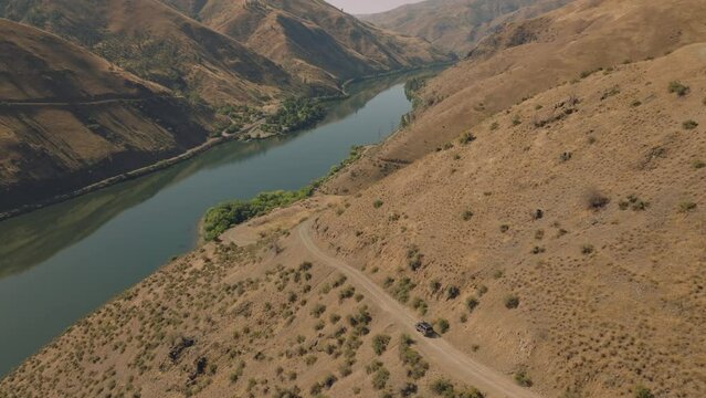 Aerial following car down scenic dirt road on side of cliff in river gorge