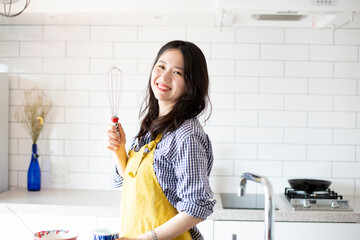 キッチンでエプロンを付けて泡立て器を持っている女性