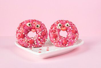 Two donuts with bright pink glaze in heart-shaped plate on pink background, Food concept of romantic love