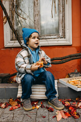 Little happy boy eating pizza, outdoors, sitting on city street.
