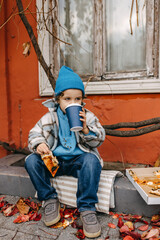 Little boy eating pizza and drinking soda, outdoors, sitting on city street.