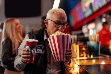 Senior man with popcorn and soda in movie theater.