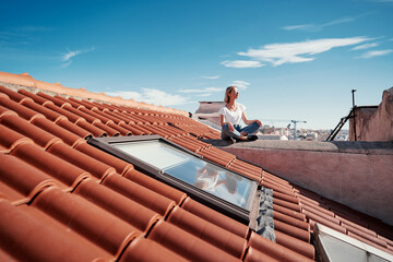 Happy young woman sitting on red tiled roof.