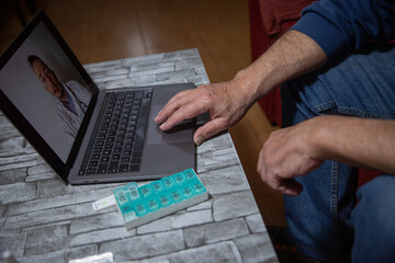 Hand of an elderly man during a video call with his general practitioner, telehealth concept