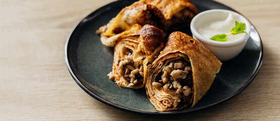 Crepes stuffed with chicken and mushrooms with sour cream on the wooden table. Banner for website.