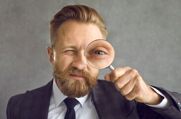 Fototapeta na wymiar Head shot handsome bearded young man in suit with magnifying glass in hand. Business expert looking for solution, hiring manager searching candidate, CEO controlling staff, entrepreneur making inquiry
