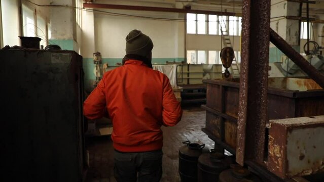  A man in an orange jacket walks through the old workshop of the factory