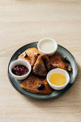 Morning breakfast concept. Delicious thin pancakes with jam, honey and sour cream on light wooden table. Copy space.