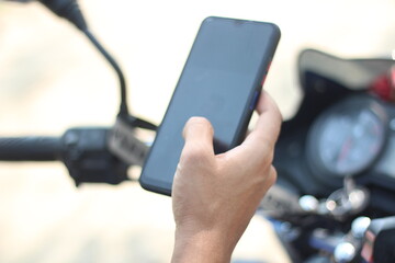 Here is a man sitting on a motorcycle holding a mobile and the background behind him is blurred