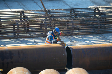A slinger moves metal pipes at a construction site. Top view real workflow. Unloading materials for...