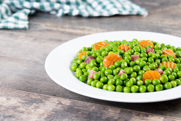 Green peas with serrano ham and carrot on wooden table. Copy space