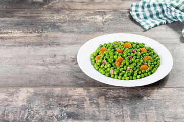 Green peas with serrano ham and carrot on wooden table. Copy space