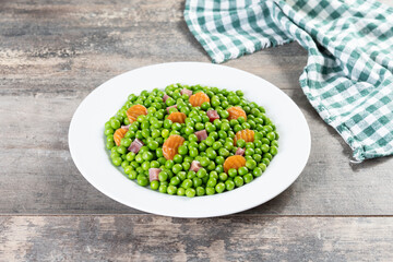 Green peas with serrano ham and carrot on wooden table.