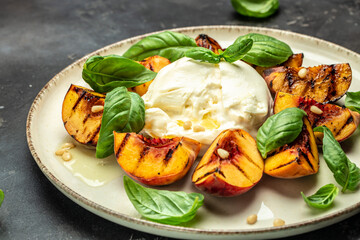 Burrata soft cheese and grilled peaches with basil and pine nuts, drizzled honey, Food recipe background. Close up