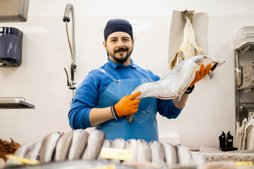 A uniformed middle-aged fishmonger is showing salmon to the camera, selling food, a concept of...