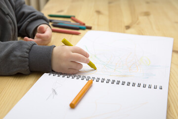Naklejka premium A baby child draws with colorful crayons in an album on a wooden table