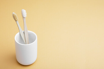 Two wooden bamboo toothbrushes in a white glass on a beige background. The concept of sustainability and the rejection of plastic. The concept of hygiene and daily routine. Copy space