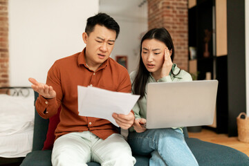Financial crisis concept. Asian couple checking documents with laptop, suffering problems with managing family budget