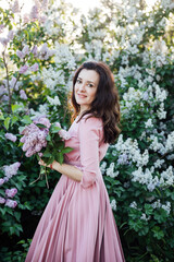 a beautiful woman in a pink dress stands with lilacs in her hands