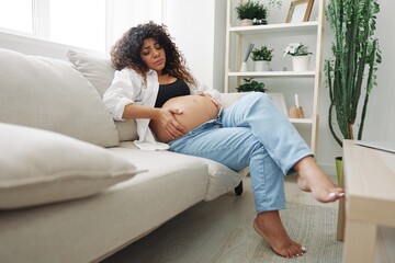 Obraz premium Pregnant woman headache lies at home in a shirt and jeans on the couch fatigue and heaviness in the last month of pregnancy before childbirth, motherhood difficulties, nausea
