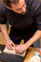 Master is making a sushi roll with nori, rice, cucumber, eel and omelet using bamboo mat