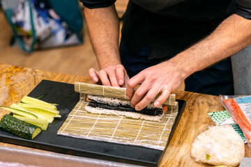 Cook's hands close-up. A male chef makes sushi and rolls from rice, red fish and avocado.