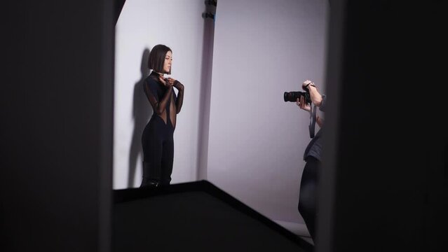 sexy young fashionable woman model in a black tight-fitting suit and leather boots is photographed in the studio with a photographer on a white background. backstage.