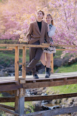 Young couple Teenage happy in the fresh beautiful Cherry pink blossom Sakura flowers full bloom in the park with a joyful vacation. Valentine's day lover of young fashion nature.