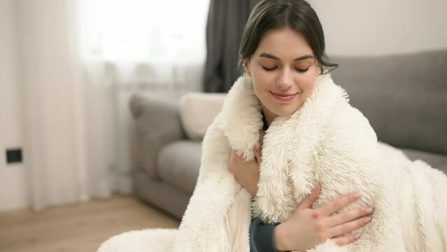 Portrait of young beautiful woman in warm fur blanket at home
