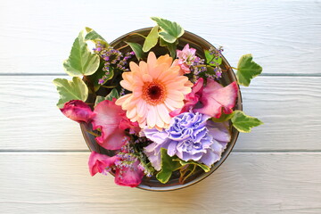 A colorful and delicate flower arrangement in a round box on the white wall background with copy...