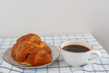 Two croissants on a white plate and a cup of black coffee on white table. Selective focus