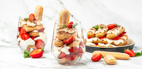 Traditional Italian dessert tiramisu with fresh strawberry, mascarpone and mint in glass on light background. Long banner format