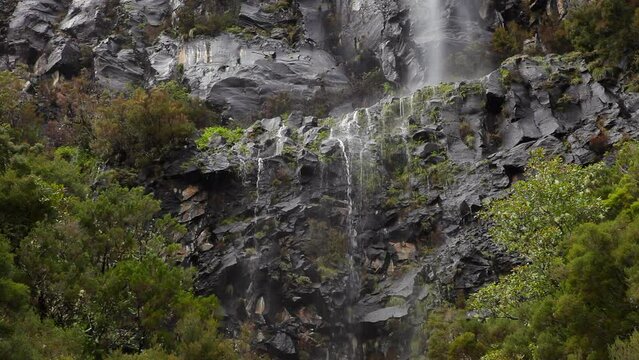 Waterfall on a rocky bluff in the mountains between trees on Madeira Island