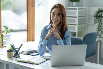 Pretty smiling Asian businesswoman sitting on camera relaxing on the desk after verifying financial documents Happy validation at the office.