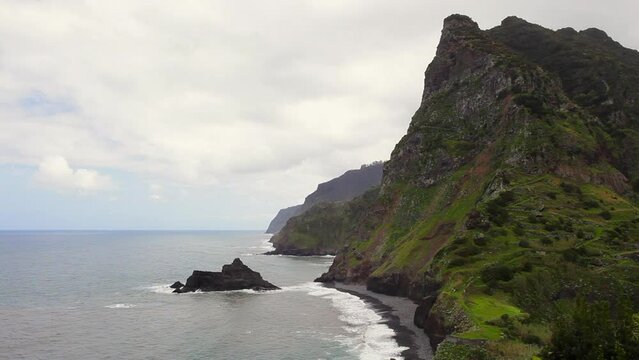 Neues calm sea off the coast of Madeira Island with green mountains against cloudy sky