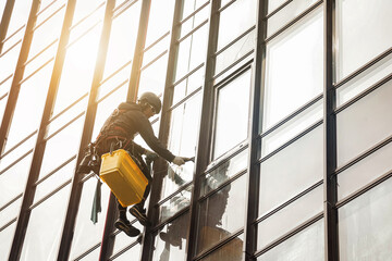 Industrial mountaineering worker hangs on facade skyscraper building, washing exterior facade...