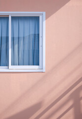 Sunlight and shadow on surface of Glass sliding window with blue curtain on pink gypsum board wall...