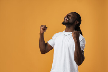 Portrait of excited african guy celebrating success with clenched fists against yellow background