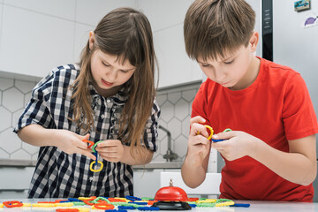 Funny school kids play toy constructor standing above kitchen table and looking down. Boy and girl...