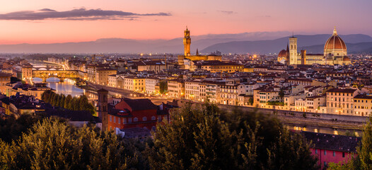 Fototapeta na wymiar The illuminated Florence cityscape with the Ponte Vecchio over Arno river, the Palazzo Vecchio and the Florence Cathedral in an orange and purple twilight.